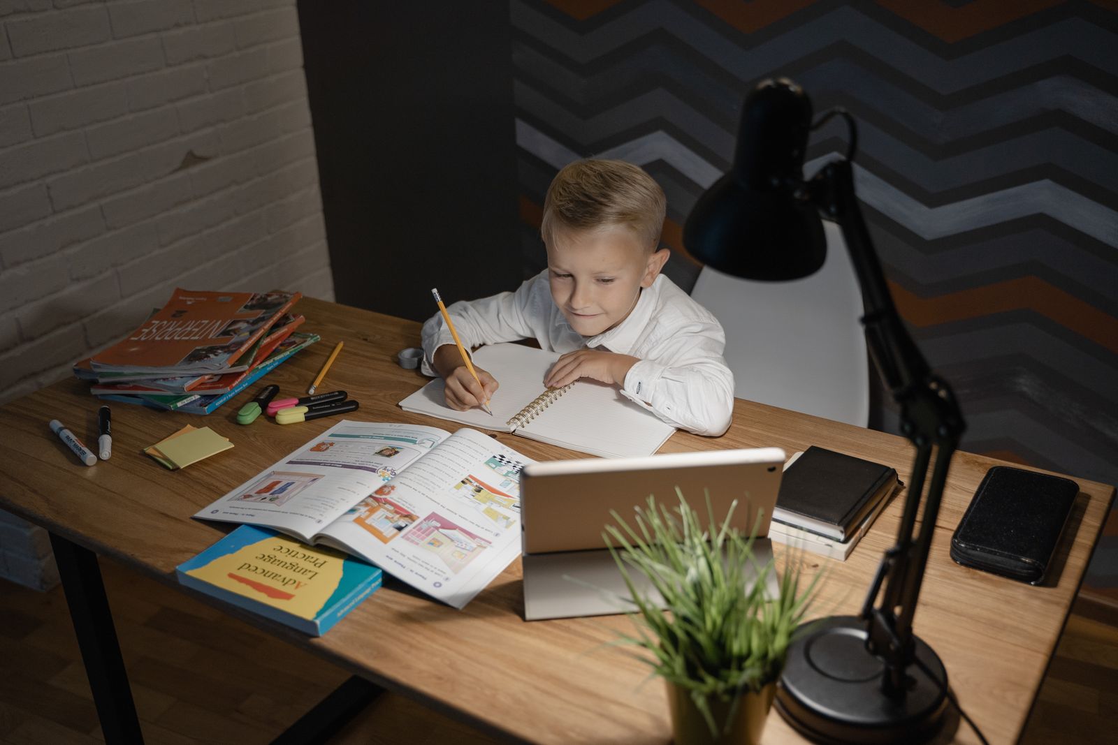 A child doing homework at a desk under a lamp in the evening